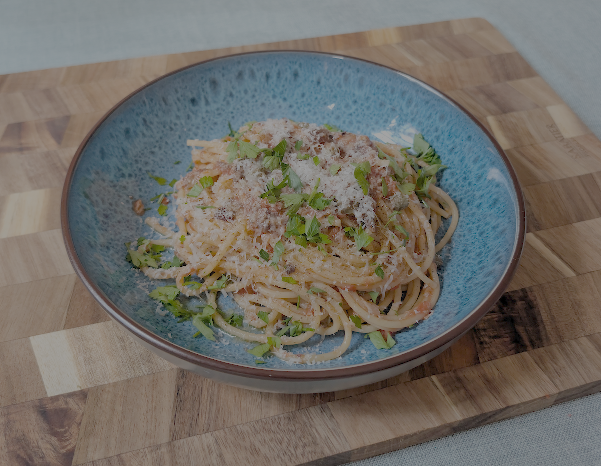 Tinned Sardine Puttanesca (tomato pasta) in blue bowl on a chopping board