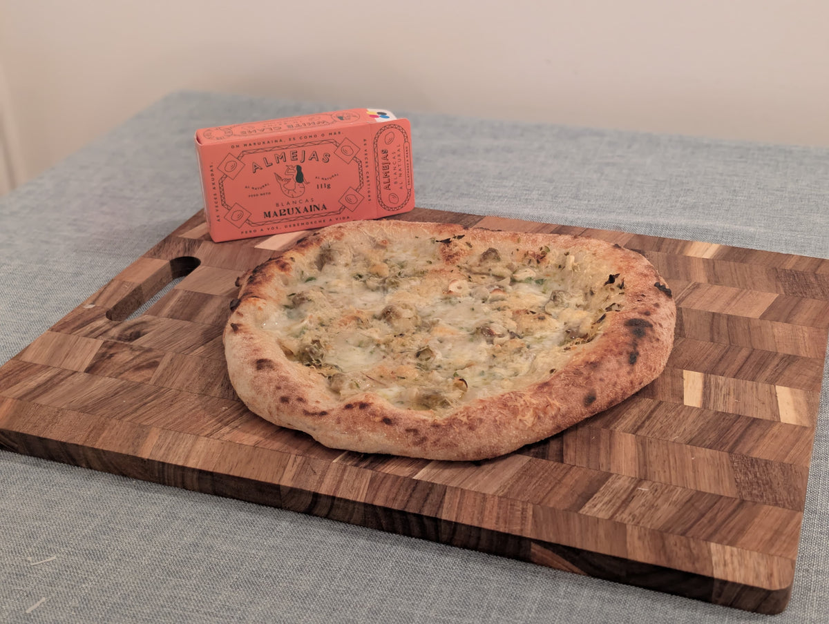 Tinned clam pizza on a chopping board, with a box of Maruxaina tinned clams next to it